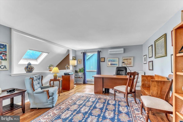 home office with vaulted ceiling with skylight, a wall mounted AC, and light hardwood / wood-style flooring