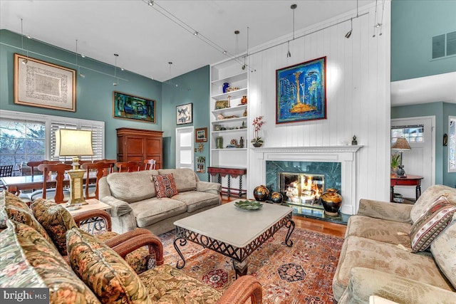 living room featuring built in shelves, a high end fireplace, hardwood / wood-style floors, and a high ceiling