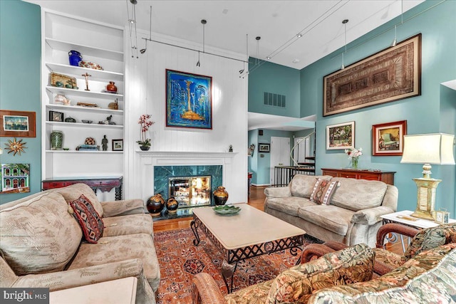 living room with a high ceiling, hardwood / wood-style floors, built in features, and a fireplace