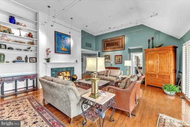 living room with a premium fireplace, vaulted ceiling, track lighting, and light hardwood / wood-style floors