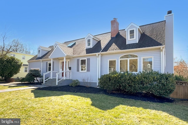 new england style home with a shingled roof, a front yard, and a chimney