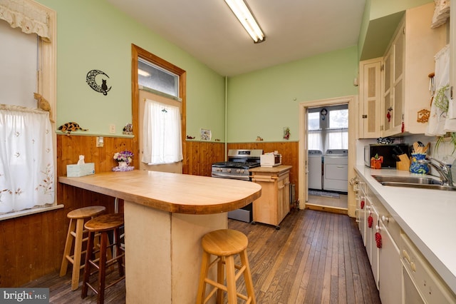 kitchen featuring light countertops, stainless steel gas range, washing machine and clothes dryer, and a kitchen breakfast bar