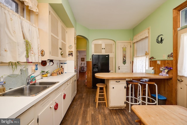 kitchen with a sink, light countertops, black fridge with ice dispenser, and a kitchen breakfast bar