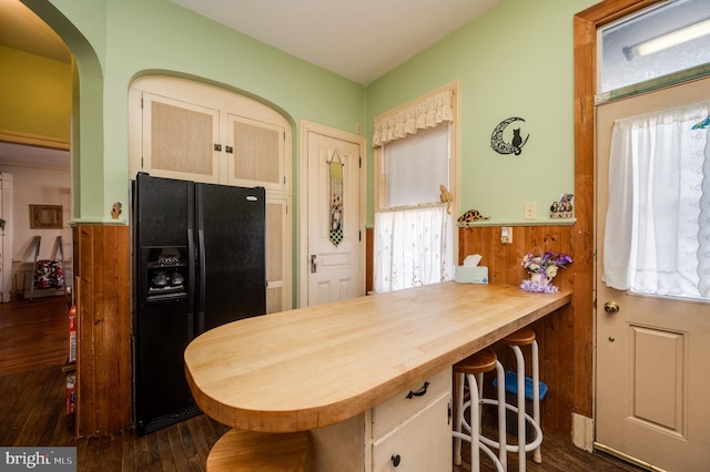 kitchen with arched walkways, dark wood finished floors, a peninsula, a kitchen bar, and black fridge