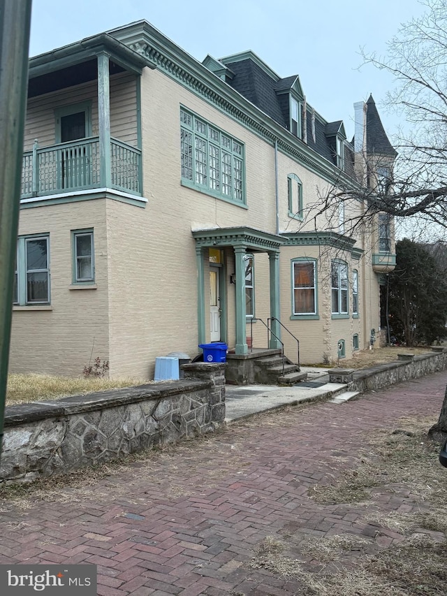 view of front facade featuring a balcony, mansard roof, and brick siding