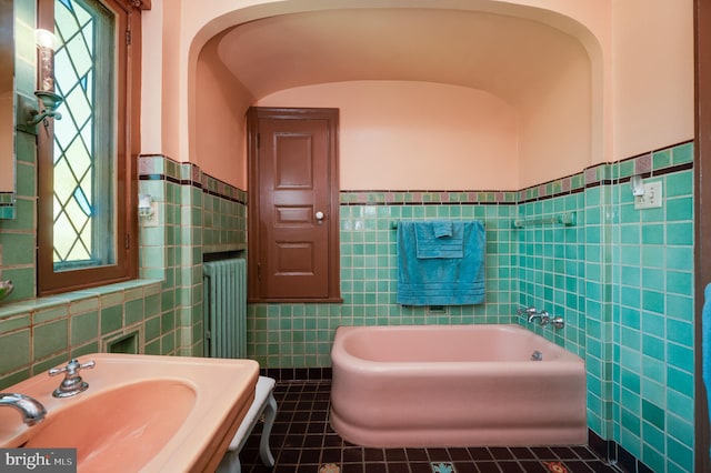 bathroom featuring a garden tub, tile patterned flooring, a sink, tile walls, and radiator