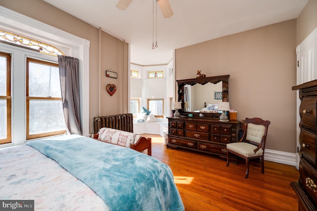 bedroom with radiator heating unit, dark wood finished floors, a ceiling fan, and baseboards