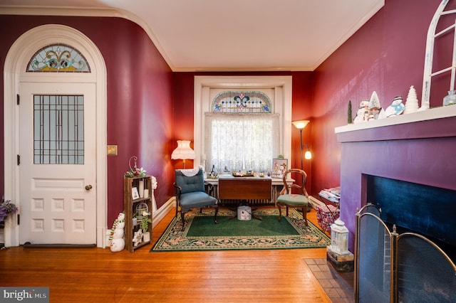 living area with baseboards, wood finished floors, a fireplace with flush hearth, and crown molding