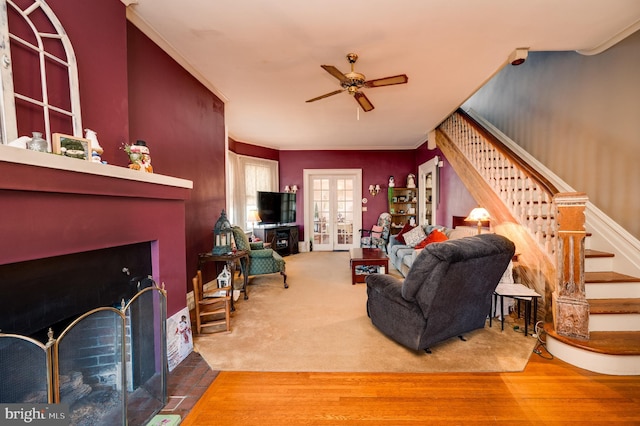 living room with ceiling fan, wood finished floors, a fireplace with flush hearth, stairs, and french doors