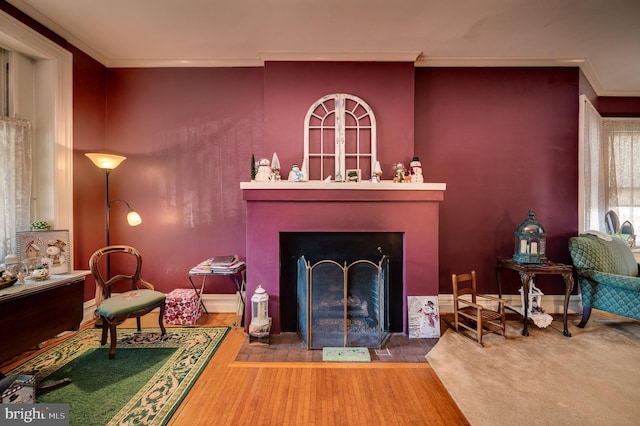 living area featuring a fireplace with flush hearth, wood finished floors, and crown molding