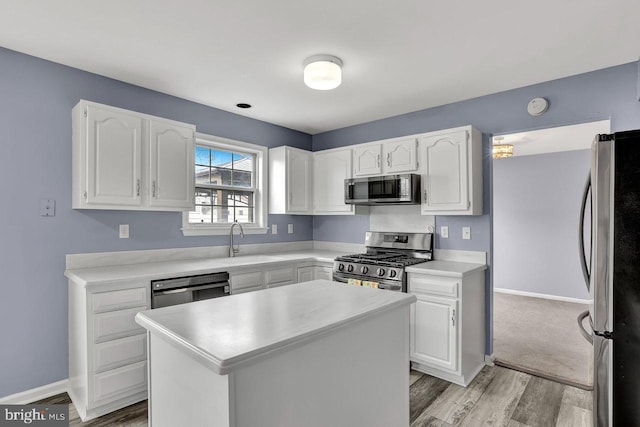 kitchen with appliances with stainless steel finishes, sink, white cabinets, a center island, and light hardwood / wood-style flooring