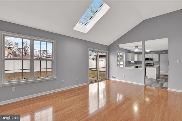 unfurnished living room featuring vaulted ceiling with skylight and light hardwood / wood-style flooring