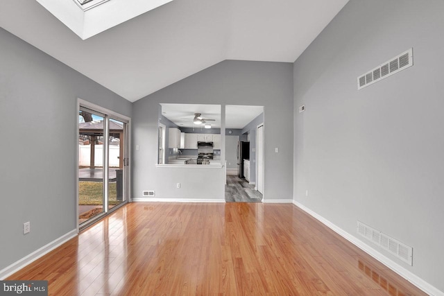 unfurnished living room featuring ceiling fan, lofted ceiling with skylight, and light hardwood / wood-style floors