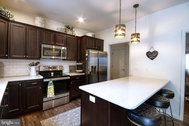 kitchen featuring a breakfast bar area, backsplash, dark hardwood / wood-style flooring, hanging light fixtures, and stainless steel appliances