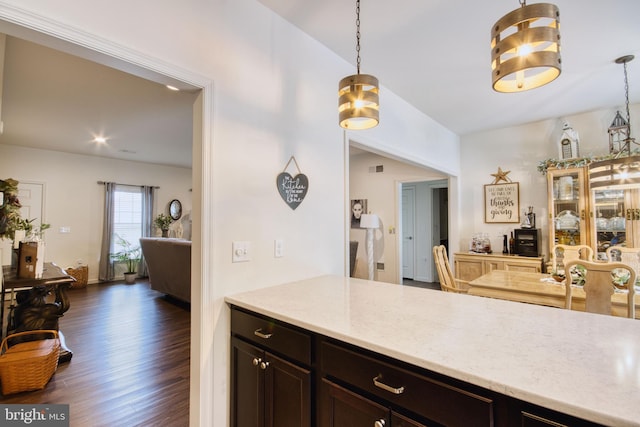 kitchen featuring light stone counters, decorative light fixtures, dark wood-type flooring, and dark brown cabinets