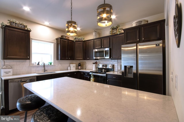 kitchen with sink, hanging light fixtures, stainless steel appliances, light stone counters, and tasteful backsplash