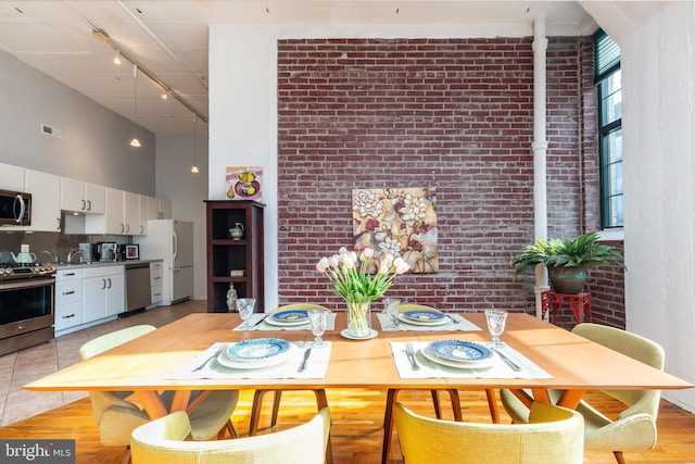 dining area with a towering ceiling, brick wall, track lighting, and light hardwood / wood-style flooring