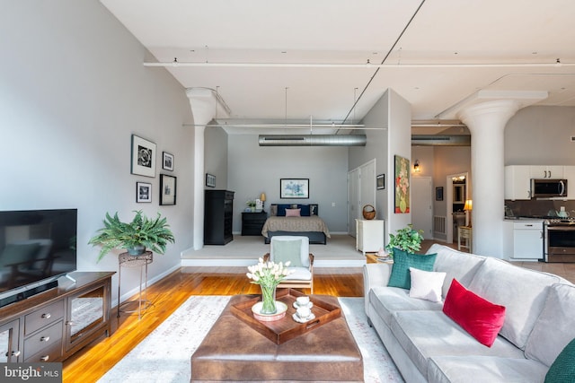 living room featuring a towering ceiling, decorative columns, and light wood-type flooring