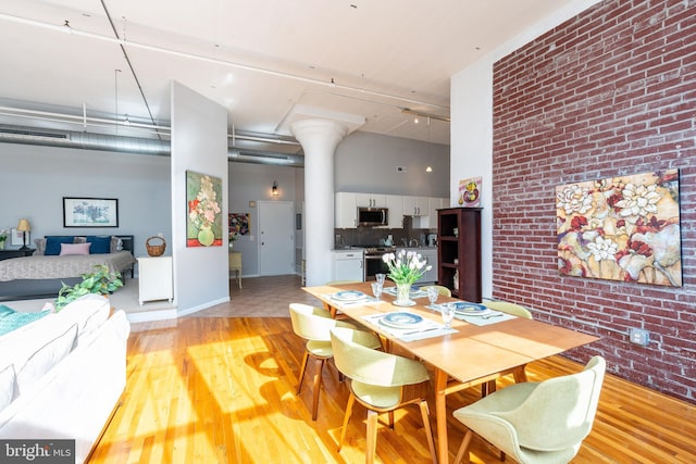 dining room featuring a towering ceiling, light hardwood / wood-style flooring, ornate columns, and brick wall