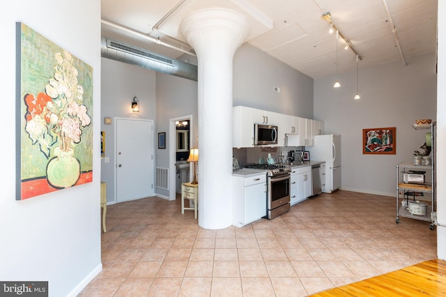 kitchen featuring light tile patterned floors, a high ceiling, white cabinets, and appliances with stainless steel finishes