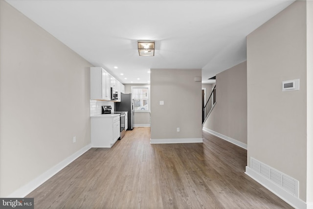 interior space with backsplash, light hardwood / wood-style flooring, white cabinets, and appliances with stainless steel finishes