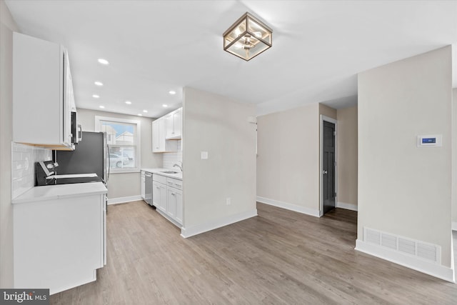 kitchen featuring range, light wood-type flooring, stainless steel dishwasher, white cabinets, and backsplash