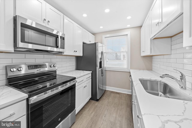 kitchen featuring sink, appliances with stainless steel finishes, light stone countertops, light hardwood / wood-style floors, and white cabinets