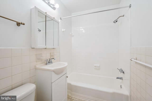 full bathroom with tiled shower / bath, tile walls, vanity, and toilet