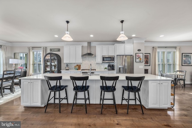 kitchen with a large island, hanging light fixtures, stainless steel appliances, and wall chimney exhaust hood