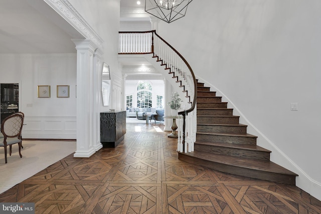 foyer with a decorative wall, a high ceiling, baseboards, stairway, and ornate columns