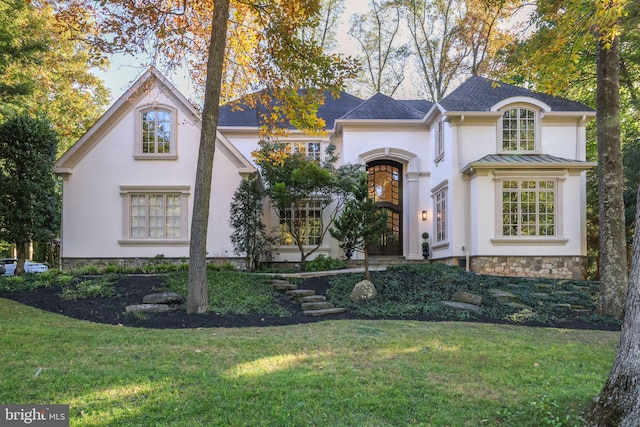 view of front of home with a standing seam roof, metal roof, a front lawn, and stucco siding