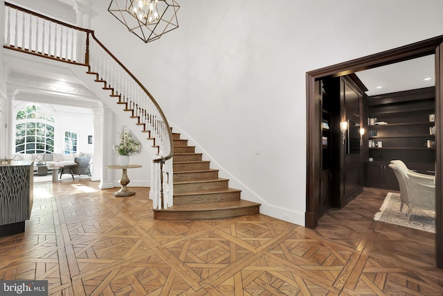 entryway featuring decorative columns, baseboards, stairs, a high ceiling, and a chandelier