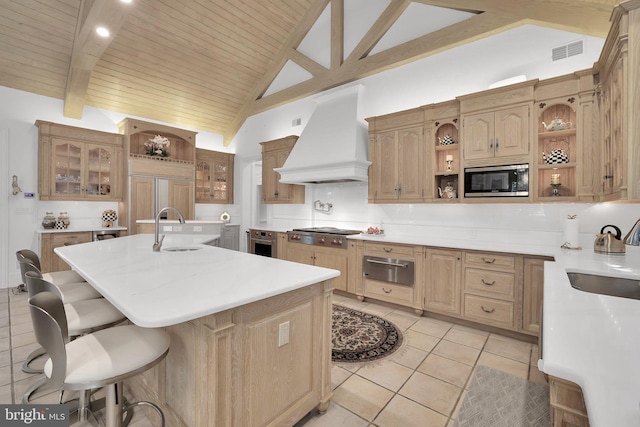 kitchen with premium range hood, a breakfast bar, light countertops, open shelves, and an island with sink