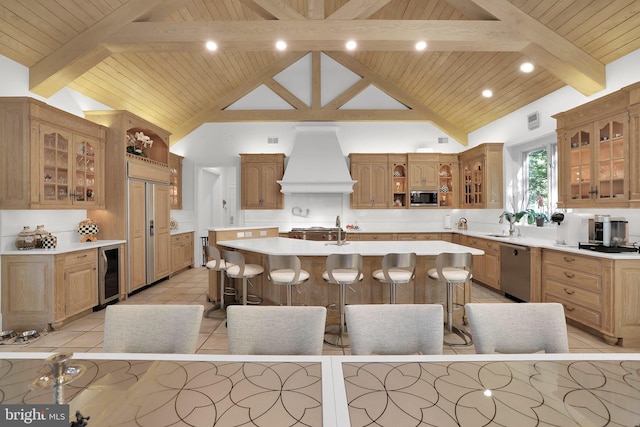 kitchen featuring glass insert cabinets, light countertops, a center island with sink, and custom exhaust hood