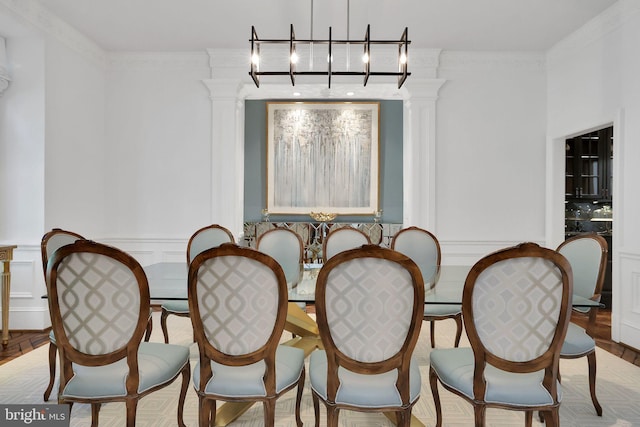 dining room featuring a wainscoted wall, ornamental molding, a decorative wall, and ornate columns