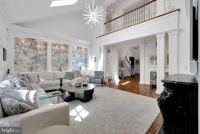 living area with a skylight, decorative columns, a chandelier, high vaulted ceiling, and stairs