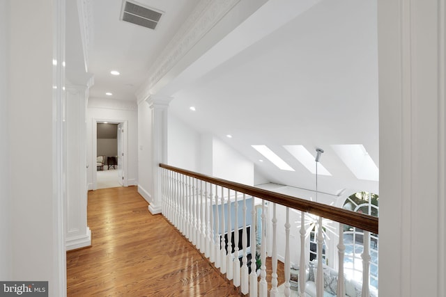 corridor featuring light wood finished floors, vaulted ceiling with skylight, visible vents, ornamental molding, and ornate columns