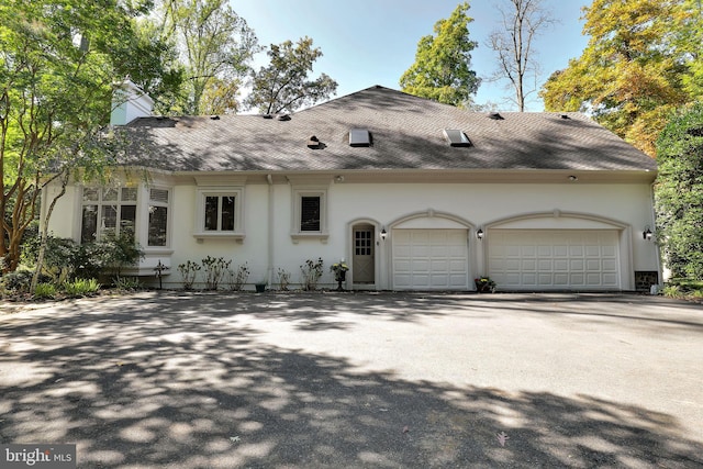 view of front facade featuring a garage, driveway, roof with shingles, and stucco siding