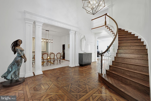 entryway featuring a towering ceiling, an inviting chandelier, stairway, and ornate columns