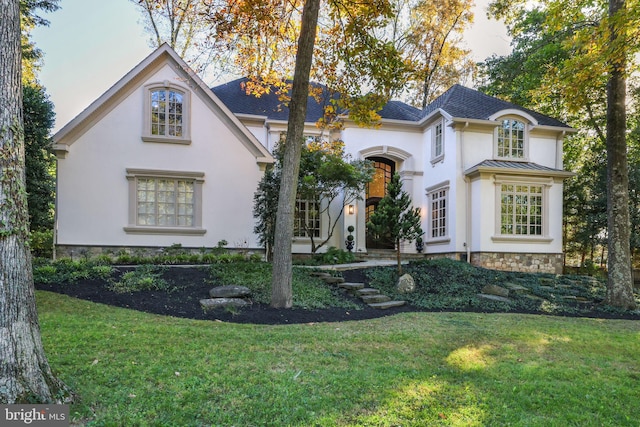 french country home featuring metal roof, a standing seam roof, a front yard, and stucco siding