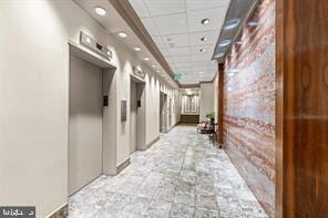 corridor featuring elevator, brick wall, mail boxes, and a drop ceiling