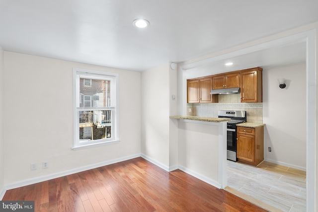 kitchen with light stone countertops, stainless steel gas range, backsplash, and light hardwood / wood-style flooring