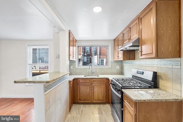 kitchen with sink, stainless steel range with gas cooktop, light stone countertops, and kitchen peninsula