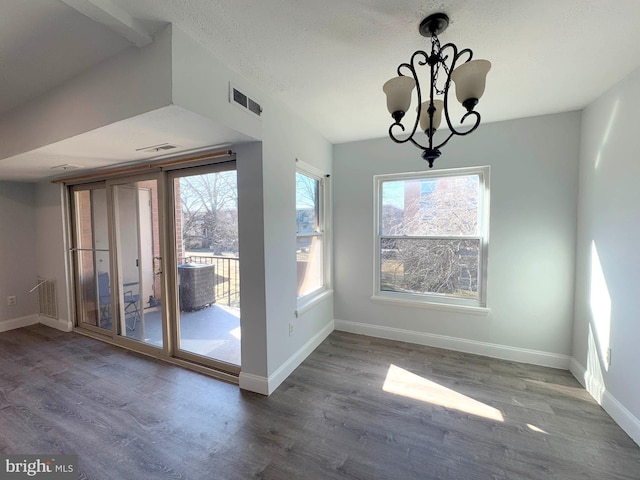 unfurnished dining area with hardwood / wood-style flooring, a healthy amount of sunlight, a chandelier, and a textured ceiling