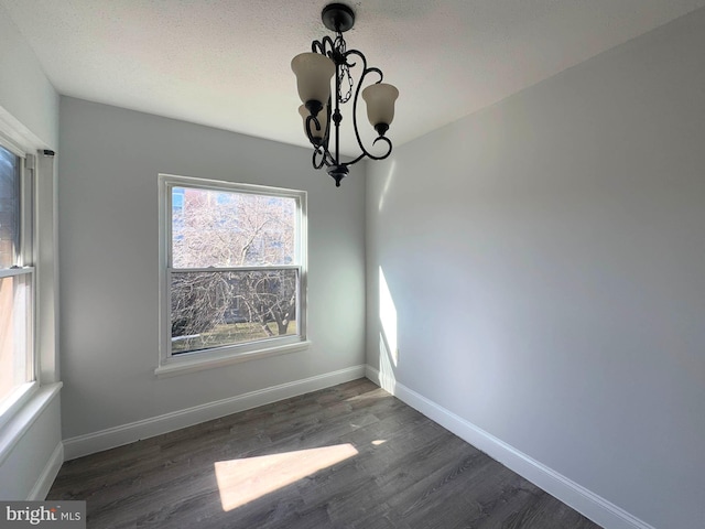 unfurnished dining area with a textured ceiling, dark hardwood / wood-style floors, and a chandelier