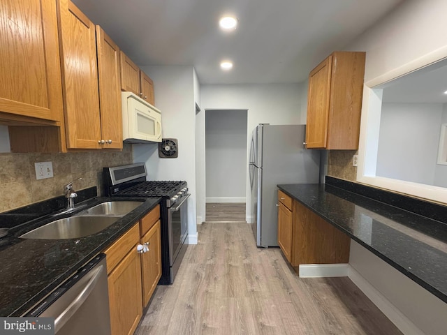 kitchen with appliances with stainless steel finishes, sink, dark stone countertops, backsplash, and light hardwood / wood-style floors