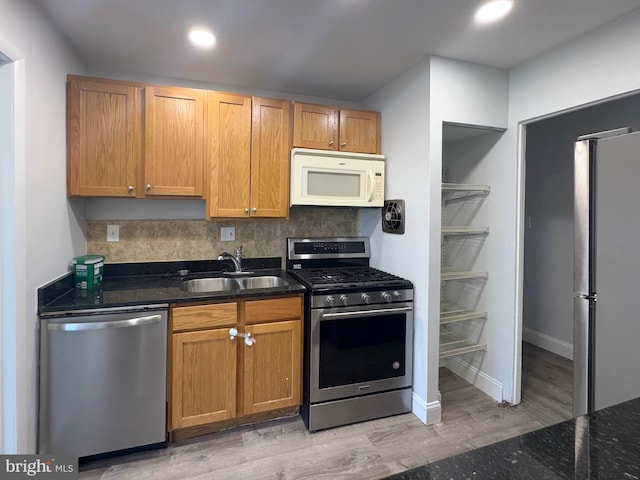 kitchen with sink, light hardwood / wood-style flooring, dark stone counters, stainless steel appliances, and decorative backsplash