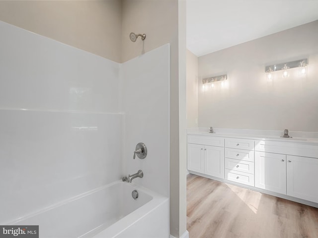 full bathroom featuring double vanity,  shower combination, a sink, and wood finished floors