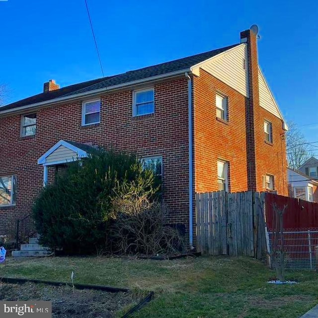 view of side of property featuring brick siding, a chimney, and fence