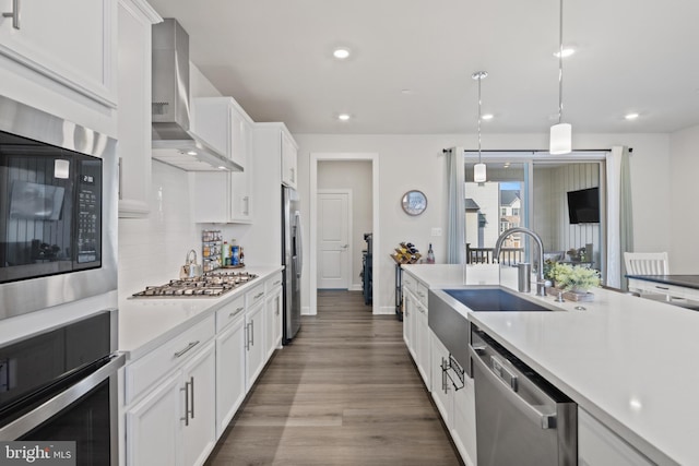 kitchen featuring white cabinets, appliances with stainless steel finishes, decorative light fixtures, and wall chimney range hood